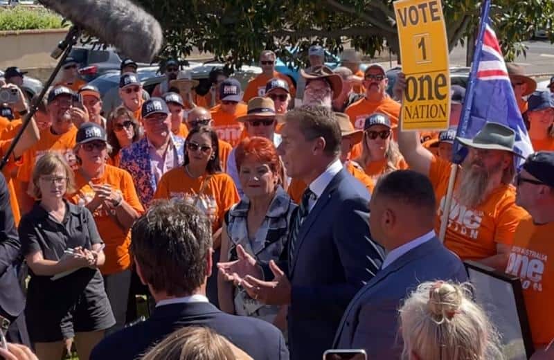 Cory Bernardi and Pauline Hanson signal poll surge while speaking to media in Adelaide with One Nation banner and an Australian flag in view. NewsBlaze image.